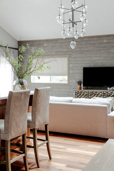 A living room featuring a couch, weathered timber walls, and high backed stools, representing a nordic interior design.