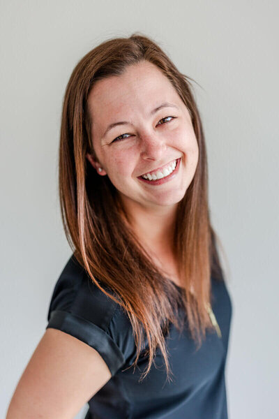 A close-up of Melissa smiling warmly at the camera, wearing a black top with a neutral background.