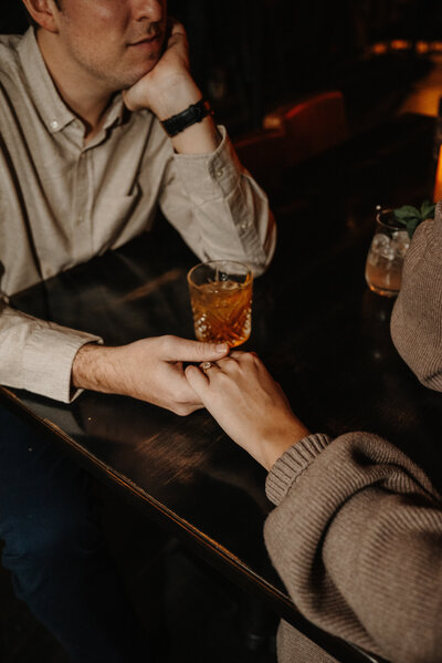 couple hold hands at a bar table in the lincoln park area of chicago while sipping on cocktails