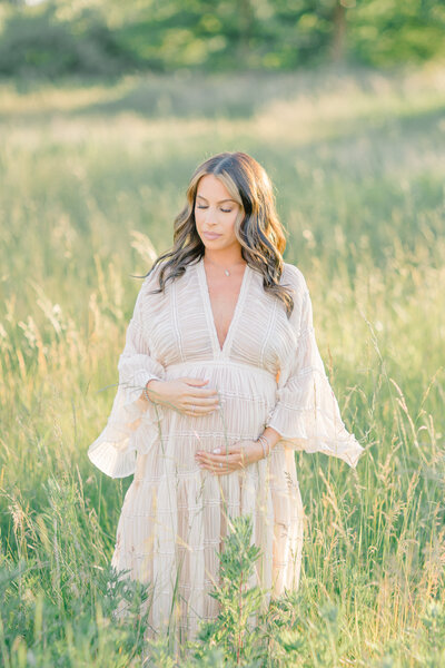 Pregnant mom standing in a field during golden hour, wearing a beautiful flowy dress, capturing a peaceful and radiant moment
