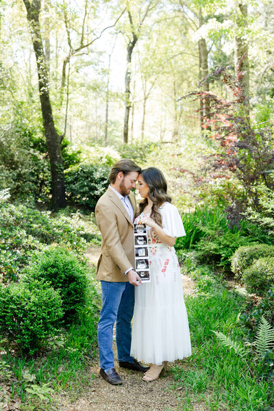 Couple posing with sonogram for maternity photography in the woods in Dothan Alabama