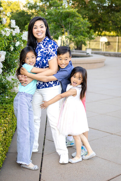 A joyful mom embracing her three smiling kids during a golden hour family session – captured by ellobelle photography.