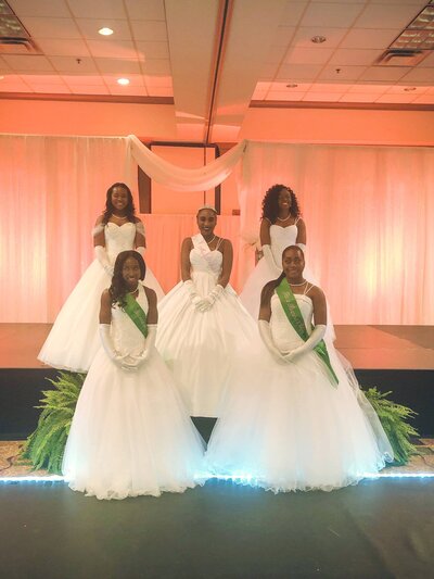 4 black young woneb wearubg white ball gowns and gloves standing on stage after a debutant ball