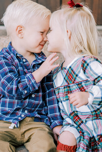 Close up image of a little boy and his sister smiling at each other with their faces touching