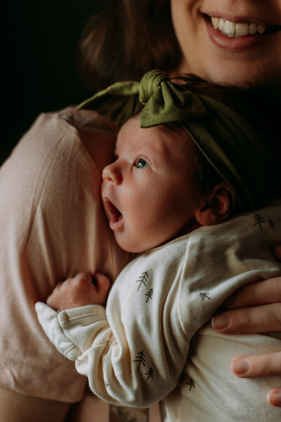 Close up of baby looking up with mouth wide as her mother holds her and smiles