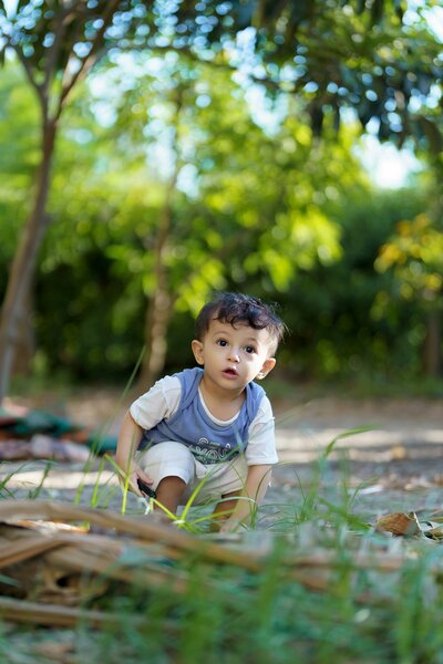 Little Latino boy engaged in early literacy and learning outside surrounded by plants and green trees, representing early childhood education in East Dallas, Dallas TX.