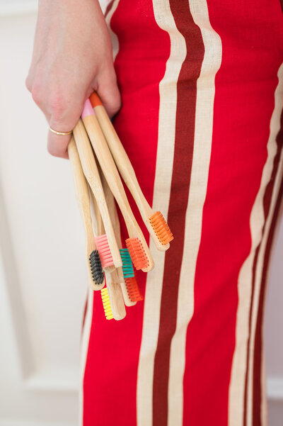 Woman in red striped pants holding colorful wooden toothbrushes