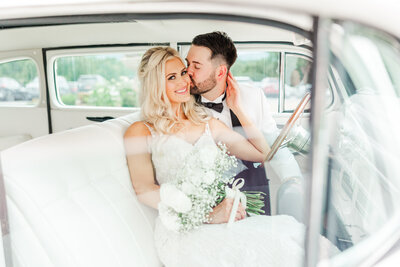 groom kissing his wife on the cheek in a vintage car