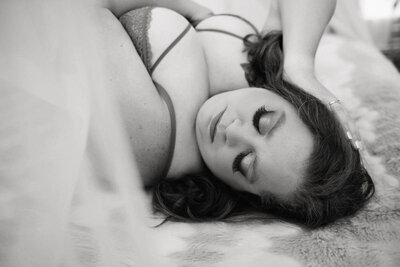 A woman lying on her back on a soft surface, eyes closed, wearing lingerie. Her hand rests on her head, conveying relaxation and tranquility. Black and white.