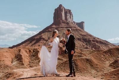 bride and groom holding hands and looking at each other while standing in the desert