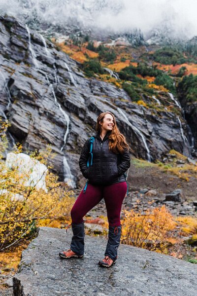 woman in burgundy leggings smiling off camera with waterfalls behind her