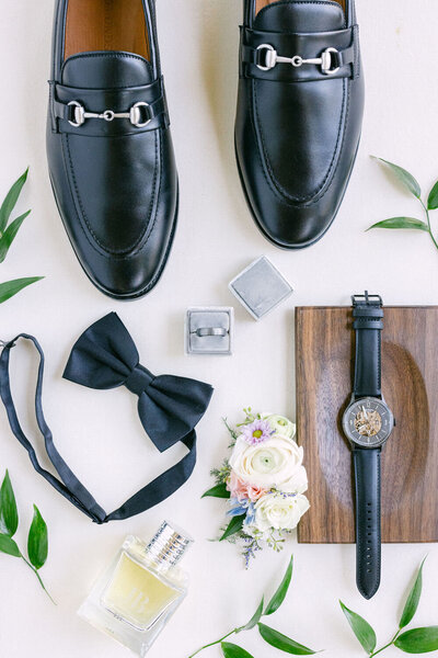 A sophisticated lay-flat photograph of the groom’s wedding day essentials, featuring shoes, rings, watch, and other elegant details, captured in timeless style before he gets ready.