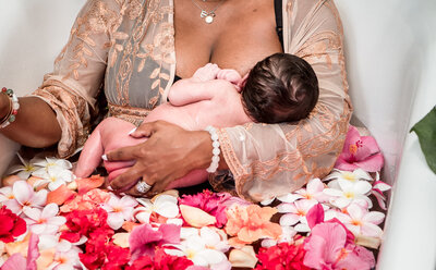 Mother breastfeeding newborn in a floral milk bath, symbolizing nourishment and postpartum healing