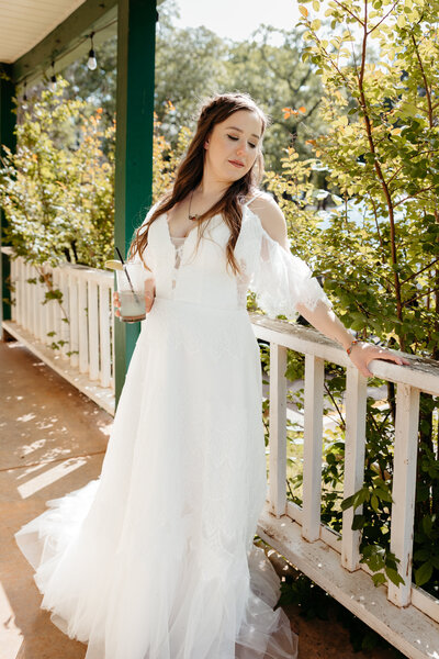 A bride leaning up against a white porch railing.