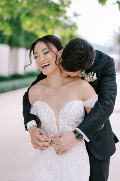 Groom hugging bride from behind while laughing, romantic wedding portrait by photographer from Toronto