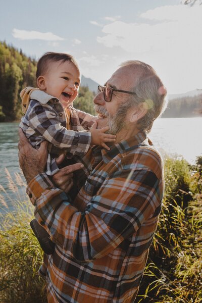 A grandpa holds up his grandson during golden hour in Cooper Landing, Alaska