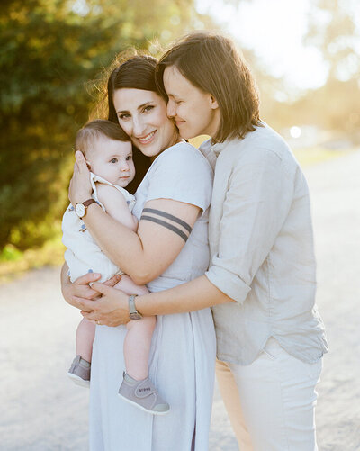 Two moms hugging with their baby during their family photoshoot at Jericho Beach