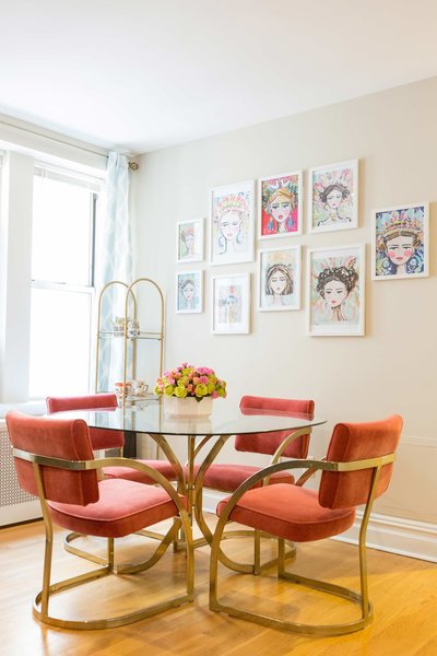 A glass table with orange in gold chairs  and paintings of empowering women.