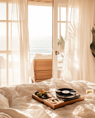 Record player on soft bedding beside an open window with an ocean view, capturing the quiet intimacy of healing and self-reflection