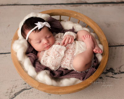 baby girl newborn in a lace onesie comfortably sleeping posed in a round basket during her newborn session