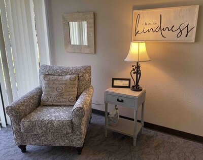 This photos shows one view of Sheri Zanganeh's Roseville office interior, with a patterned armchair, end table, and a sign reading "Choose Kindness."