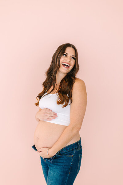 Woman holding her pregnant belly and smiling in front of a pink background