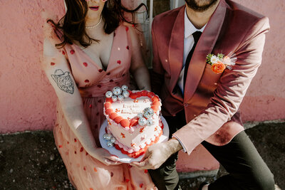 Two people holding a small heart shaped cake together 