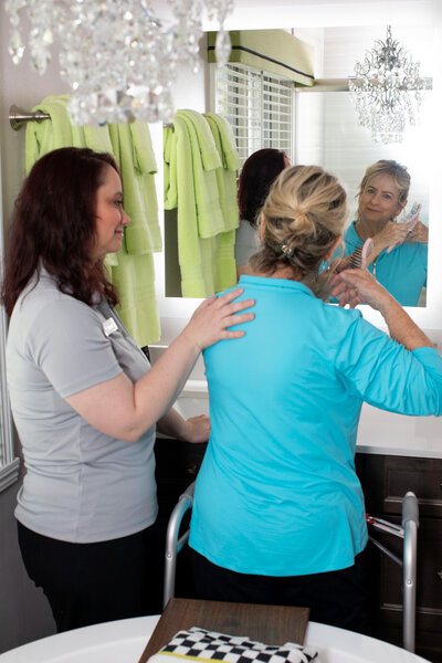 Caregiver gently assisting senior woman with brushing her hair at home
