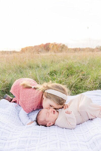 girl kisses baby brother  during outdoor newborn photo session with Sara Sniderman Photography in Natick Massachusetts