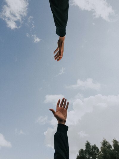 looking up to blue sky with two hands reaching towards one another