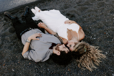 bride and groom laying on black sand beach in northern minnesota