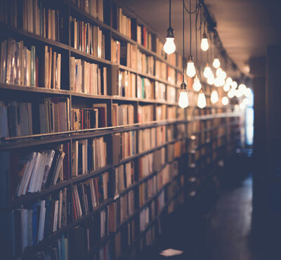 A row of library shelves curves into the distance, warmly lit by hanging lightbulbs.