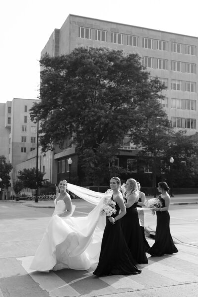 Bridal party walking across the street while holding the bride's train, captured by a Madison wedding photographer.