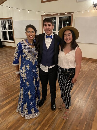 a photo of a bride wearing an indian traditional blue dress, man with a tuxedo, and a woman with a white and blue outfit and a hat