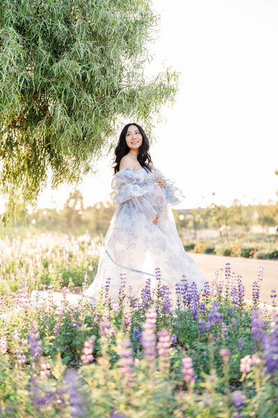 Pregnant woman with white dress exposing her pregnant belly and standing in an open field