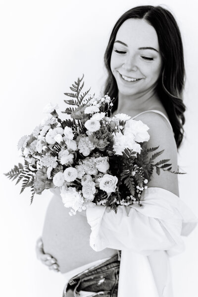 Black and white photo of woman holding a bouquet of flowers with her hand on her pregnant belly