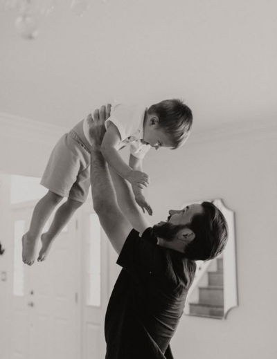 Father holding his son up in the air, smiling for a moment captured on camera