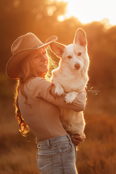 Hondenfotografie tijdens golden hour. Vrouw die corgi hond vast heeft tijdens een hondenfotoshoot op een outdoorlocatie in Nijlen. 