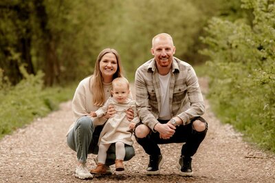 mom, dad, and little boy in an embrace with both parents kissing each cheek of the little boy in a woodland setting at a family photoshoot