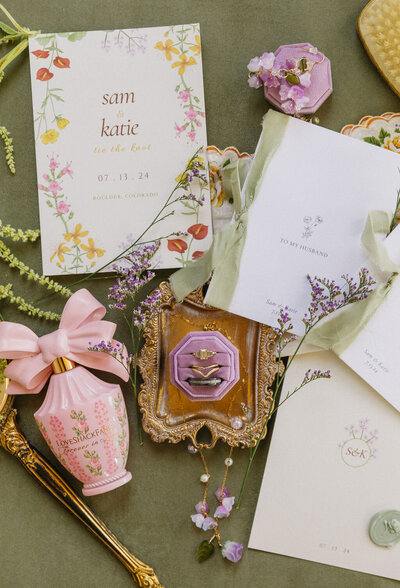 Whimsical floral wedding invitation flatlay with lavender details, stationery suite, and vintage perfume bottle for Boulder Colorado micro-wedding