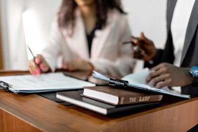 Two professionals reviewing legal documents and writing notes at a desk, symbolizing the importance of understanding the differences between state and federal ADA accessibility laws. The image supports content emphasizing the role of a Certified Access Specialist (CASp) in ensuring compliance, identifying modifications, and providing legal protection for businesses under both legal frameworks.