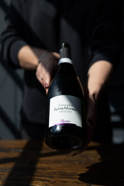 Fles Champagne van Sylvie Moreau gepresenteerd door gastvrouw Sabrina Mans in restaurant Bisque Groningen. Zon schijnt op etiket. Fotografie door Dorien Paymans | Studio Ensō Groningen ©