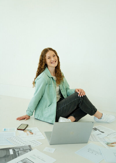 Haylee looking to the right and smiling with her computer that she designs on in front of her.