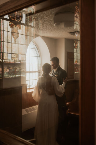a unique shot of a bride and groom standing inside a catholic church with window reflections 