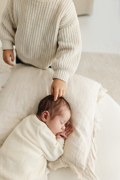 A little child points towards a newborn baby and touches the babies hair during a newborn photoshoot in christchurch with lucy jane photography
