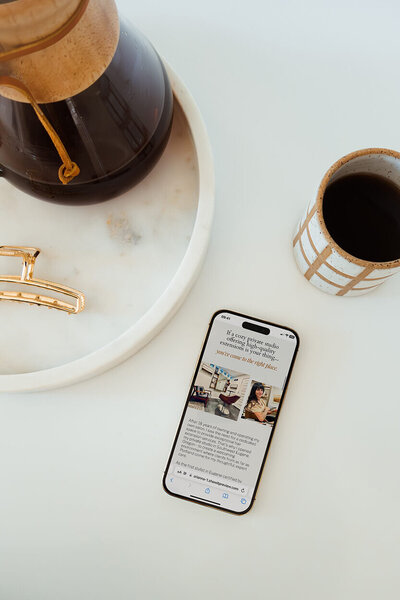 A cell phone sits on a counter by a mug of coffee, representing an example of a showit website design by Bloem Creations. 