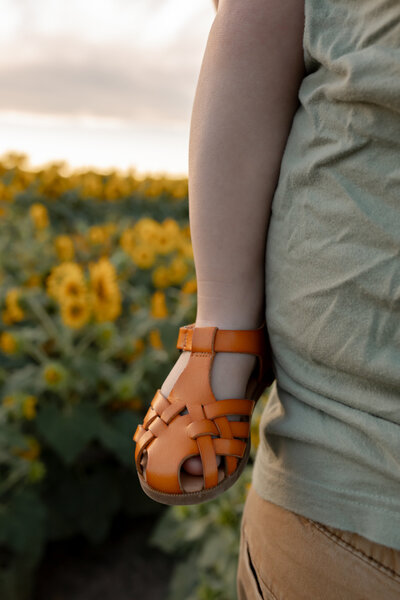 close up of a toddler's sandaled foot while being held by father in sunflower field at sunset