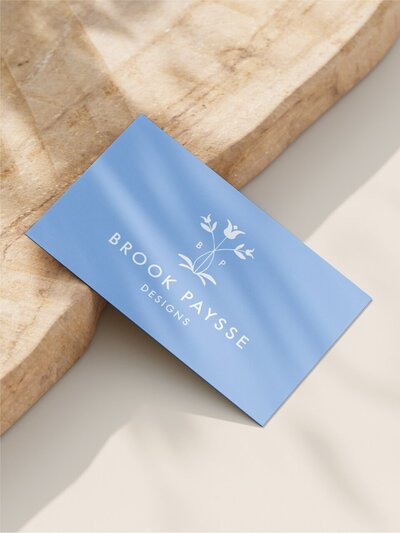 Business card featuring Brook Paysse Designs logo resting on a textured natural stone surface with soft shadows.