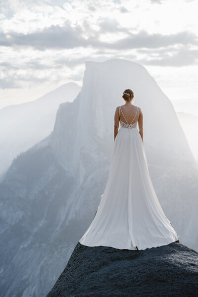 A newlywed couple with their arms around each other smiling at an overlook in Yosemite