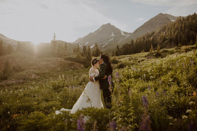 Bride and groom kiss in the Telluride mountains with wildflowers all around them